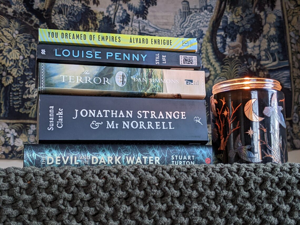 A stack of books including "You Dreamed of Empires," "Still Life," "The Terror," "Jonathan Strange & Mr. Norrell," and "The Devil and the Dark Water."