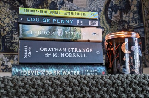 A stack of books including "You Dreamed of Empires," "Still Life," "The Terror," "Jonathan Strange & Mr. Norrell," and "The Devil and the Dark Water."